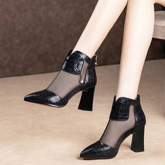 Black high-heeled shoes with mesh design worn by a person on a neutral background