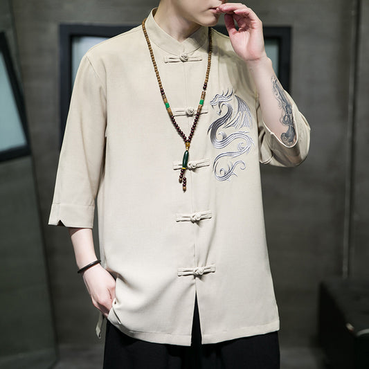 Person wearing a beige traditional-style shirt with a dragon design and a long necklace.