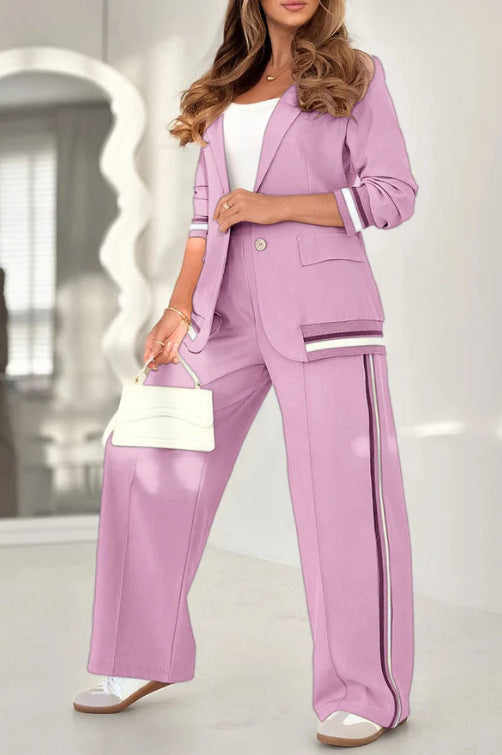 Woman wearing a lavender suit with a white top and holding a white handbag indoors.