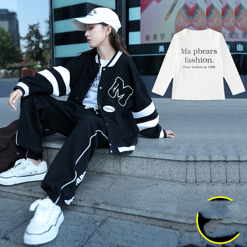 Person wearing a black and white varsity jacket with a logo, sitting on steps outdoors.