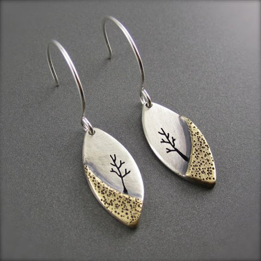 Pair of silver and gold earrings with tree design on a gray background