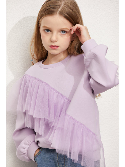 Young girl wearing a light purple sweater with ruffled layers on a plain background