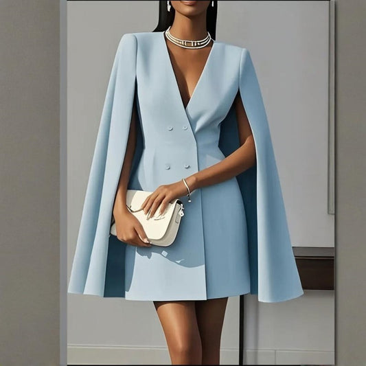 Woman wearing a light blue cape dress holding a white clutch against a neutral background