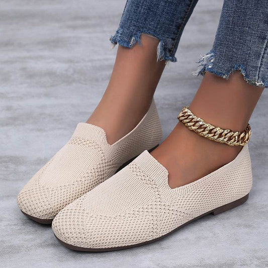 Beige knitted loafers worn with denim jeans on a gray surface