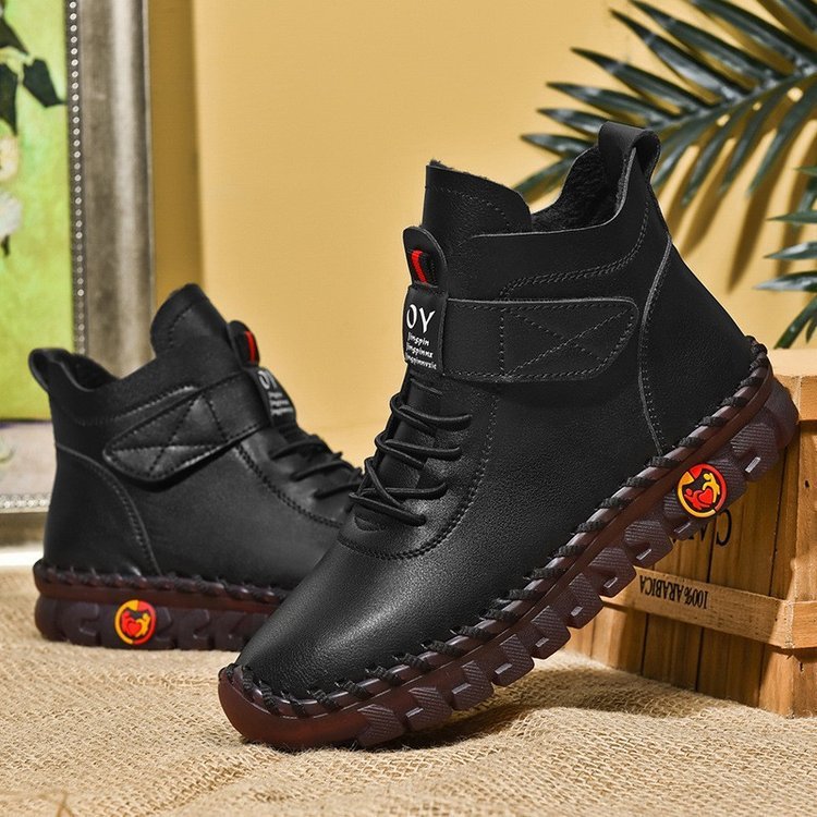 Black leather boots with brown soles on a textured surface with a plant in the background
