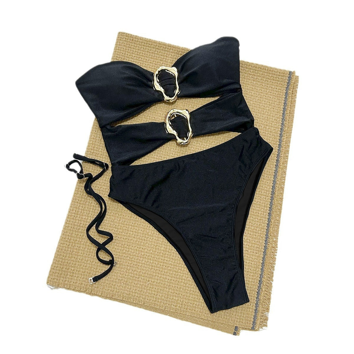 Black bikini set with gold straps on a textured beige surface