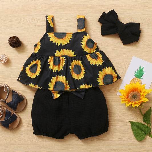 Children's outfit with sunflower pattern top and black shorts on a wooden surface.