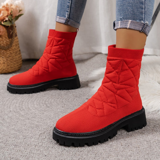 Red quilted boots with black soles worn by a person on a neutral background