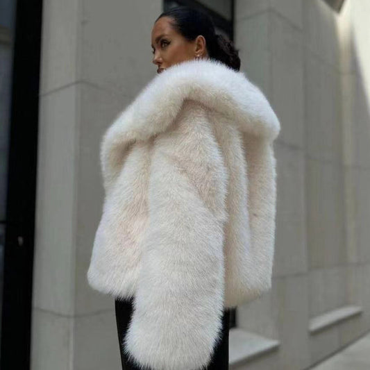 Person wearing a white fur coat standing against a neutral wall.