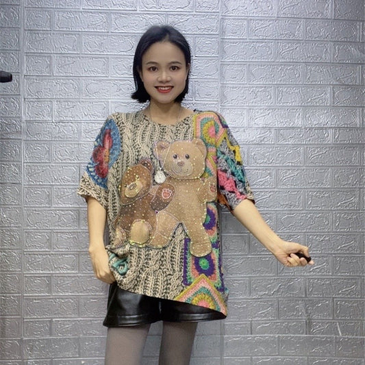Woman wearing a colorful sweater with teddy bear designs against a textured gray wall.