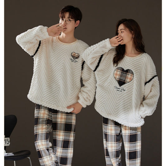 Two people wearing matching cream-colored sweaters with heart designs and plaid pants on a dark background.