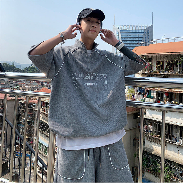 Person wearing a gray tracksuit with 'DCHX' branding on a balcony with cityscape background