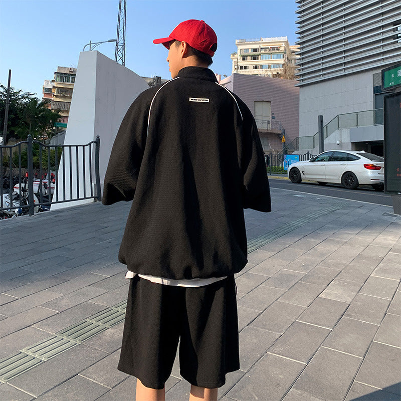 Person wearing a black outfit with a red cap on a city street.