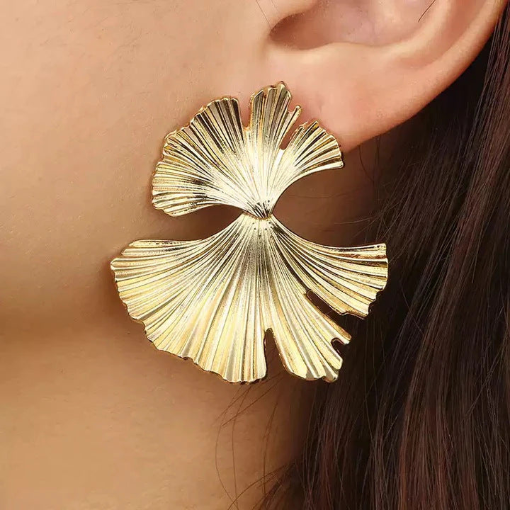 Gold leaf-shaped earring worn by a person with dark hair.