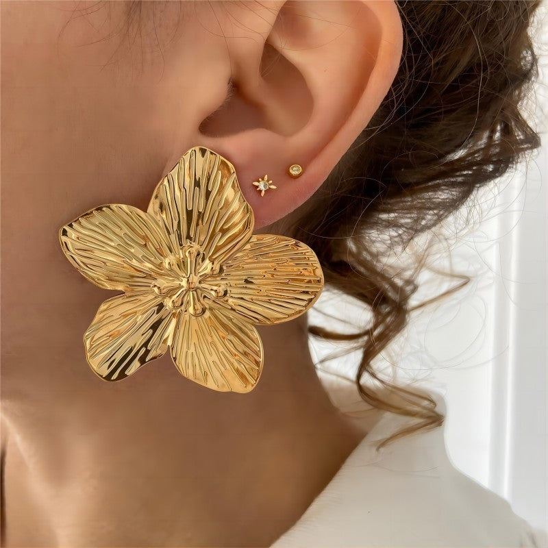 Gold flower-shaped earring worn by a person with a blurred background
