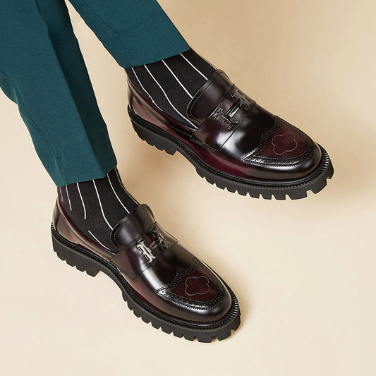 Dark brown leather shoes with striped socks and green pants on a beige background
