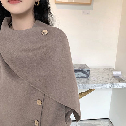 Person wearing a brown poncho with buttons in an indoor setting