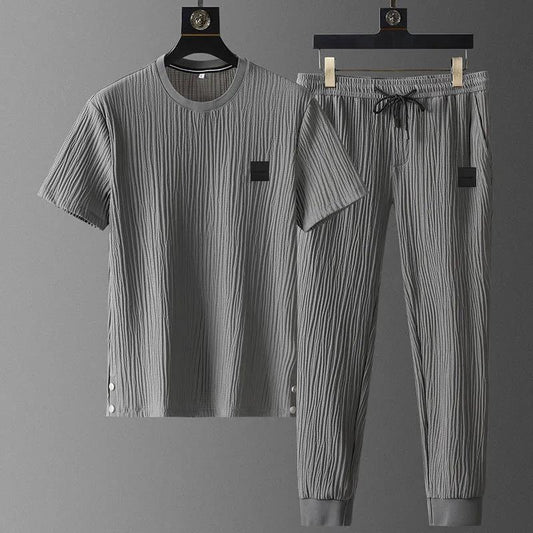 Gray pleated outfit with shirt and pants on hangers against a gray background