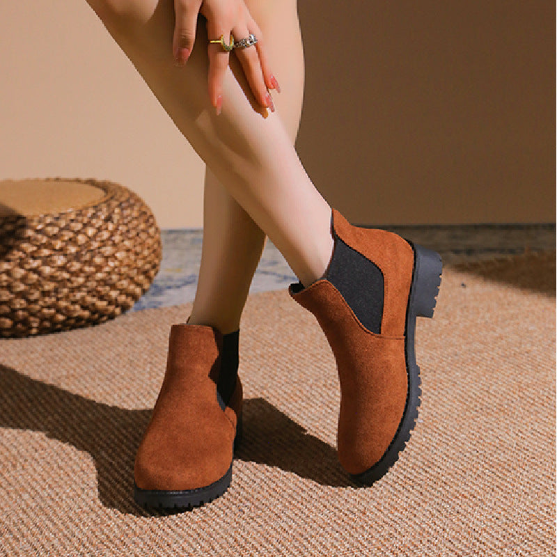 Brown ankle boots worn by a person on a textured surface with a woven mat in the background.