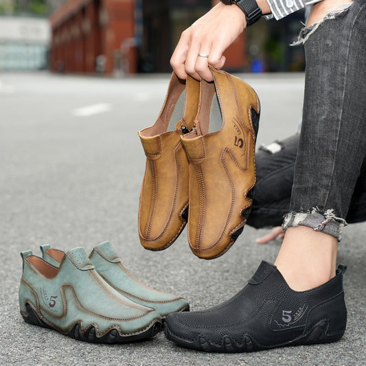 Person holding a pair of brown shoes with two other pairs of shoes on the ground.