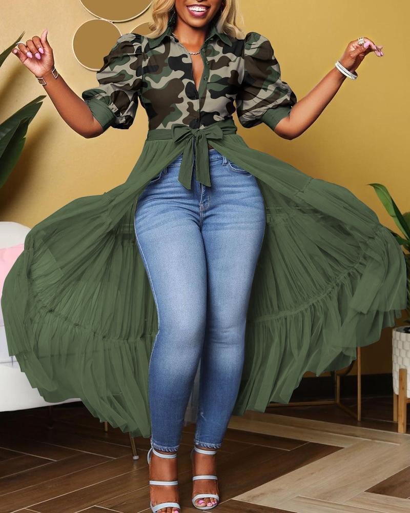 Woman wearing a camouflage top and green long coat with blue jeans indoors.