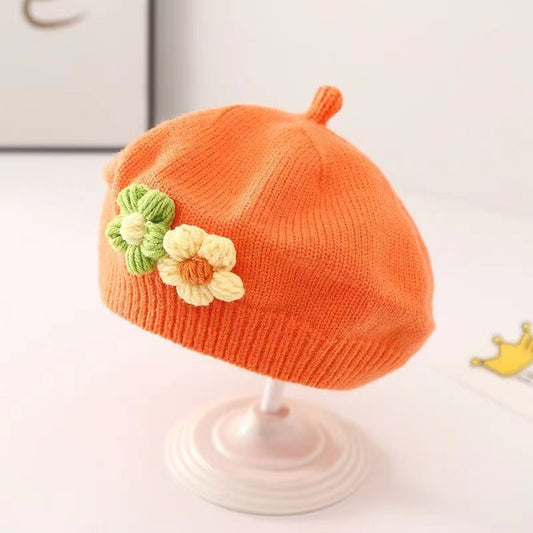 Orange knit baby hat with flowers on a white stand