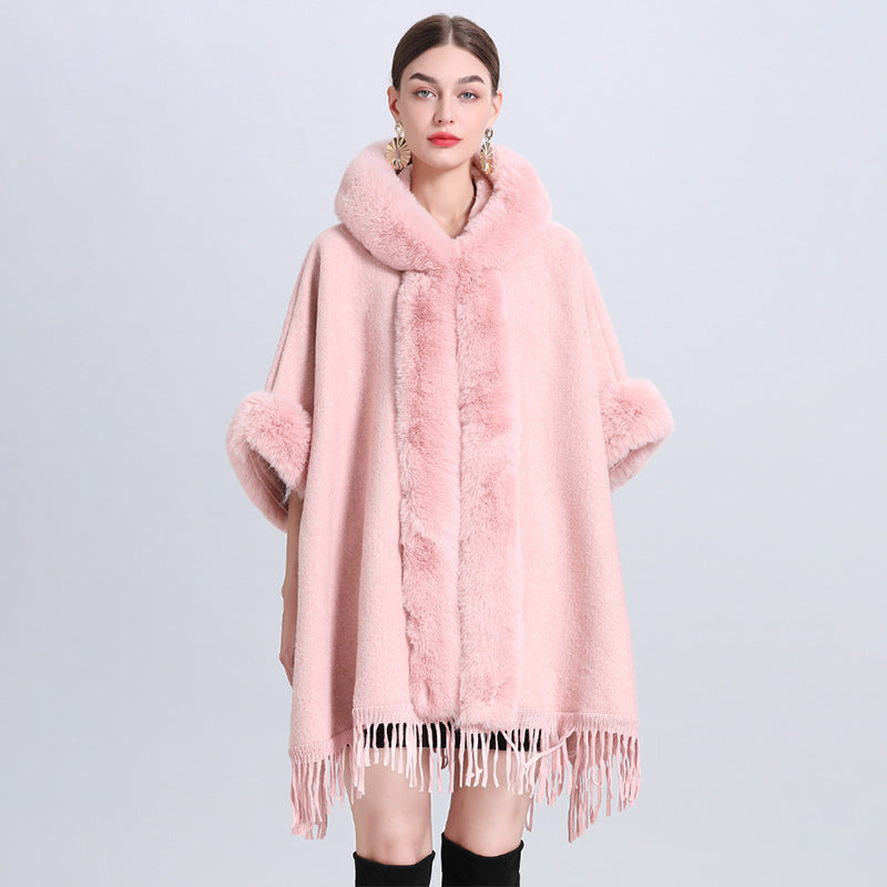 Pink poncho with fur trim worn by a model on a light gray background