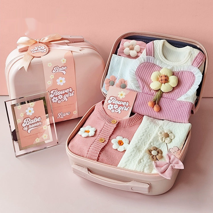 Pink baby outfit with floral details in an open suitcase on a pink background