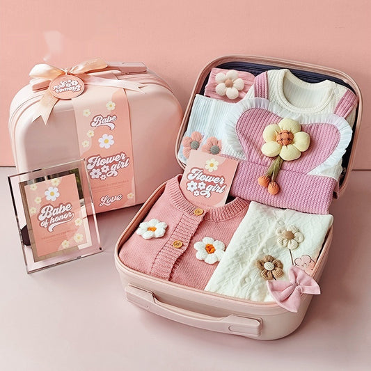 Pink baby outfit with floral details in an open suitcase on a pink background