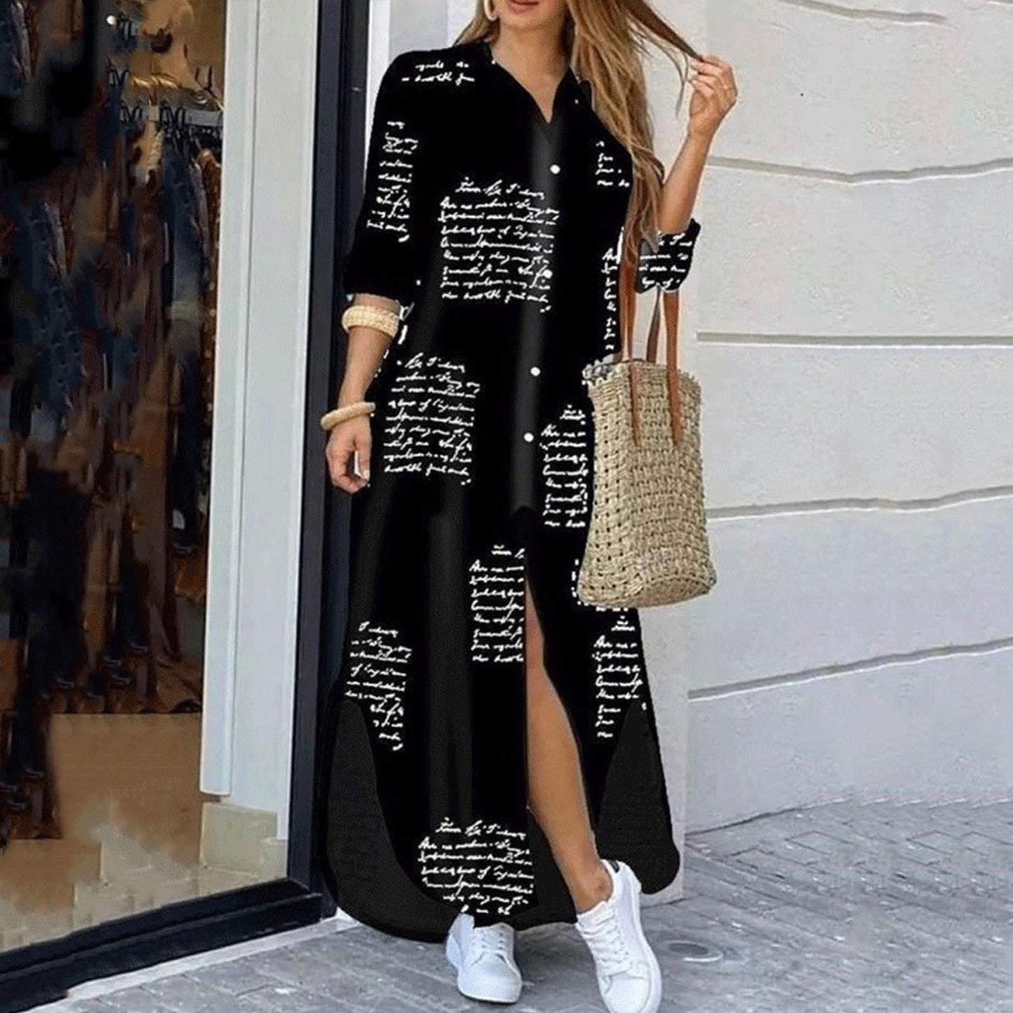 Woman wearing a long black dress with white text pattern, standing outside a store.