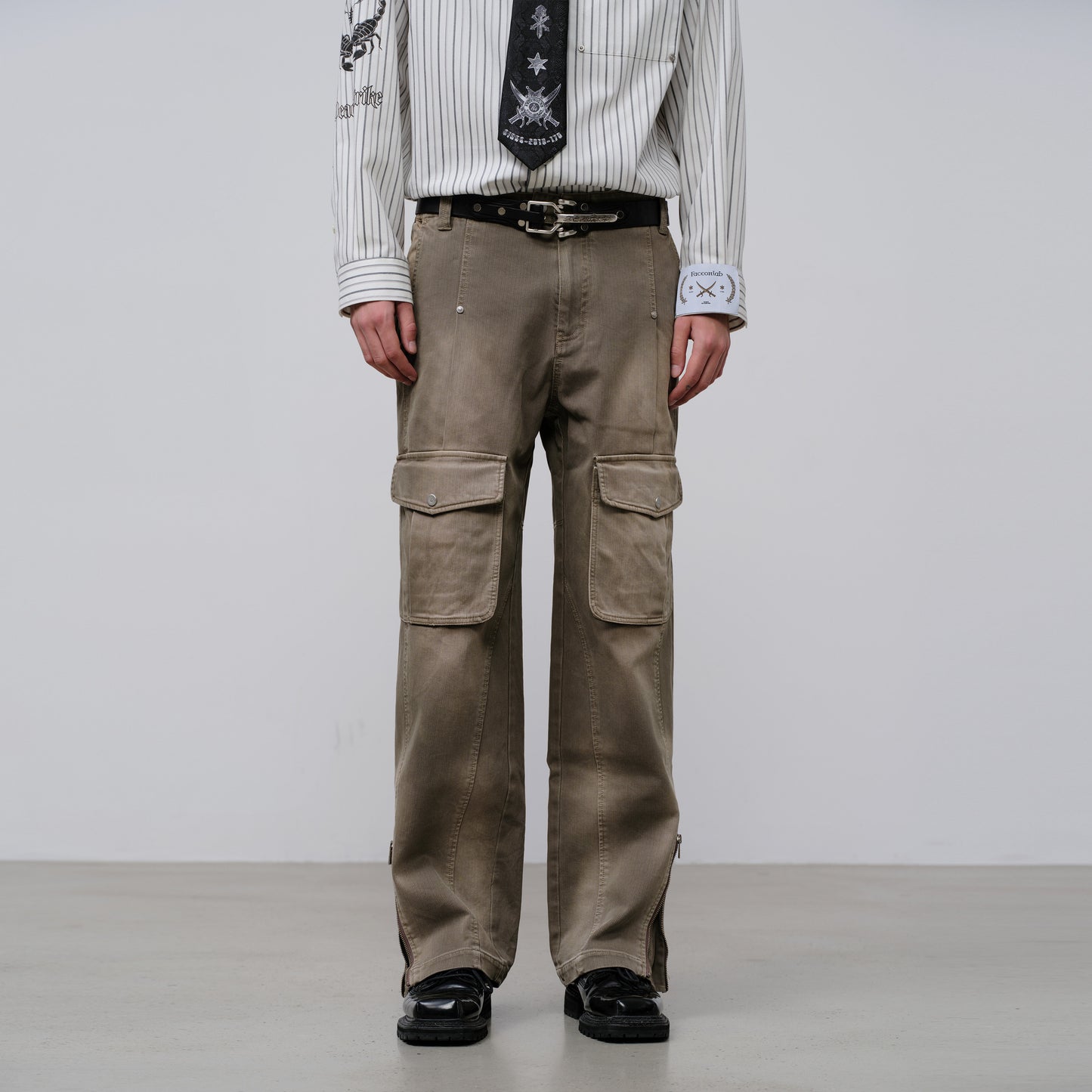 Person wearing brown cargo pants with a white shirt and black shoes on a plain background
