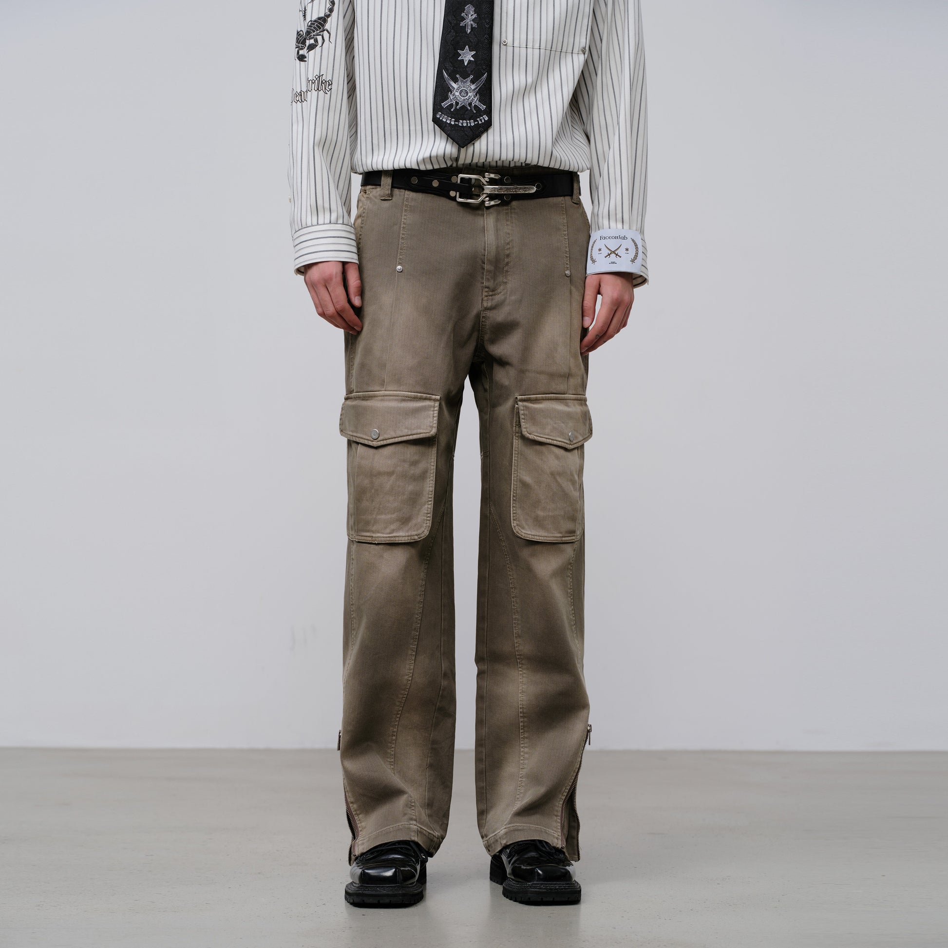 Person wearing brown cargo pants with a white shirt and black shoes on a plain background