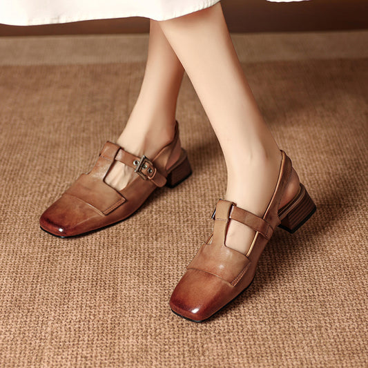 Brown shoes with buckles worn by a person on a textured brown surface
