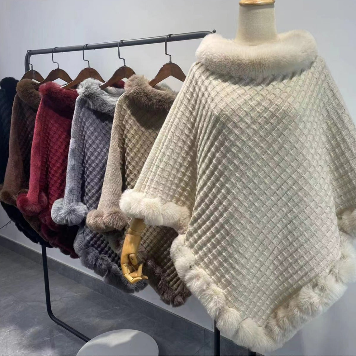 Collection of various textured ponchos on a rack with a white background