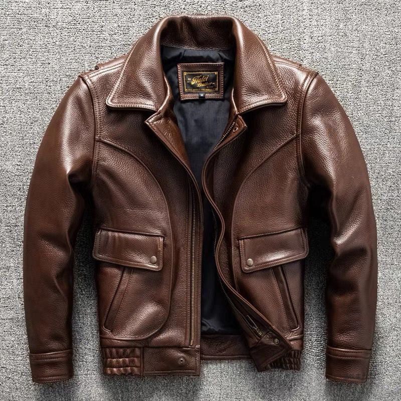 A brown leather jacket with a pointed collar, front zipper, and flap pockets, laid flat on a gray textured background.
