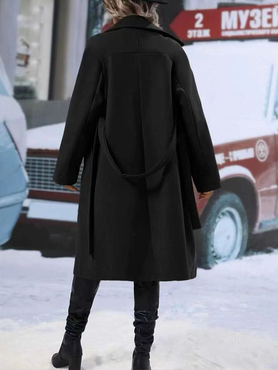 Person wearing a black coat in an urban setting with snow on the ground.