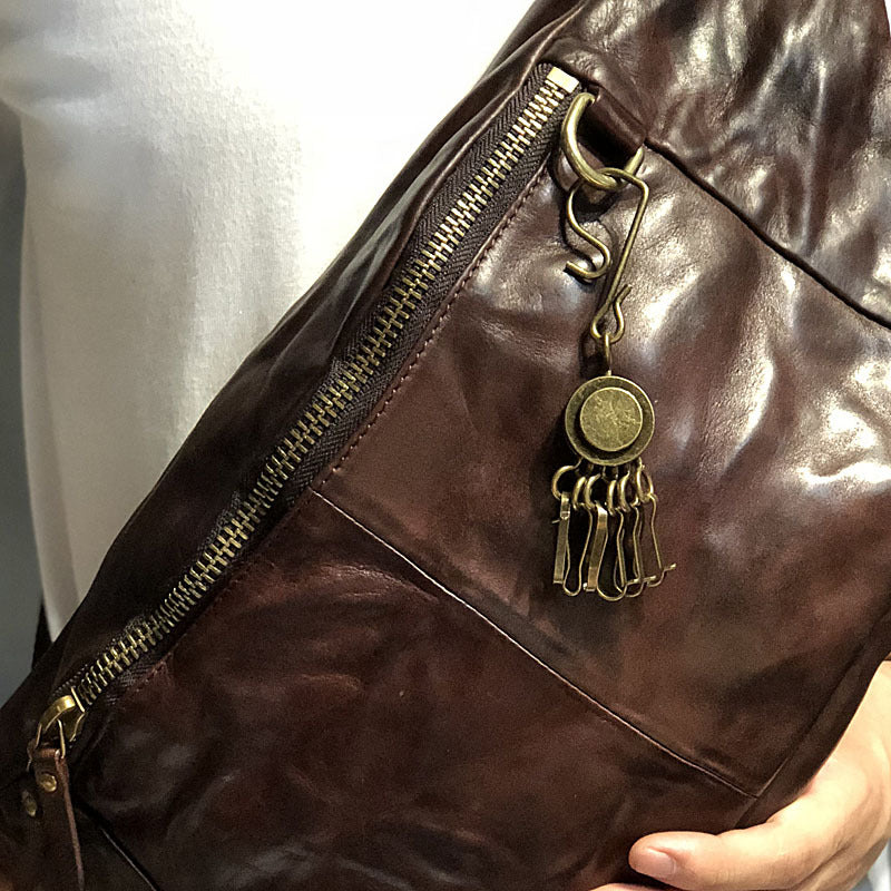 Brown leather bag with a gold keychain featuring a circular pendant and hanging elements.
