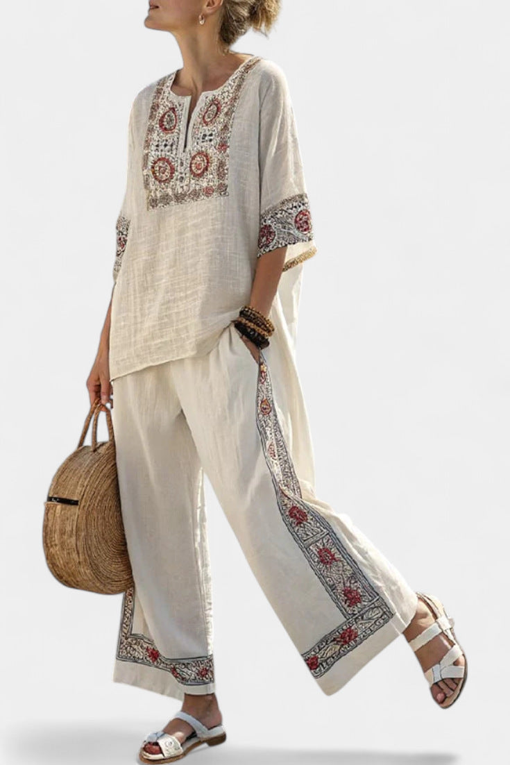 Woman wearing a white outfit with red and black patterns, holding a woven bag against a light background.