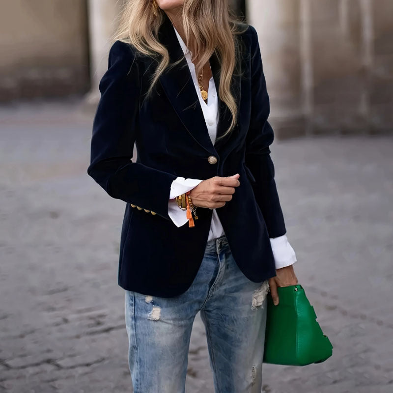 Person wearing a navy blazer, white shirt, and blue jeans, holding a green handbag.