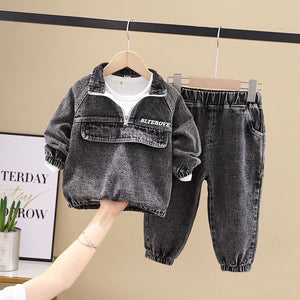 Children's black denim jacket and pants set on a hanger against a beige wall.