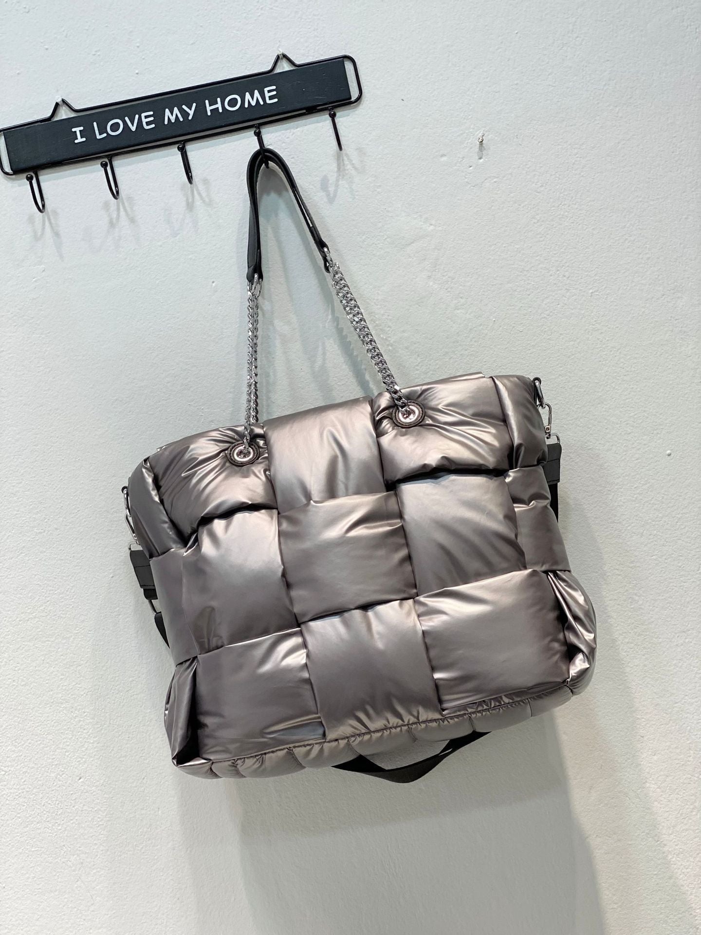 Silver quilted handbag hanging on a wall hook with 'I Love My Home' sign.