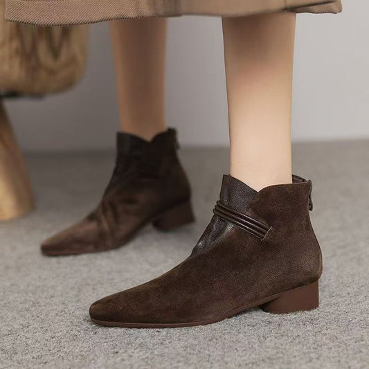 Brown suede ankle boots worn with a beige coat on a neutral background