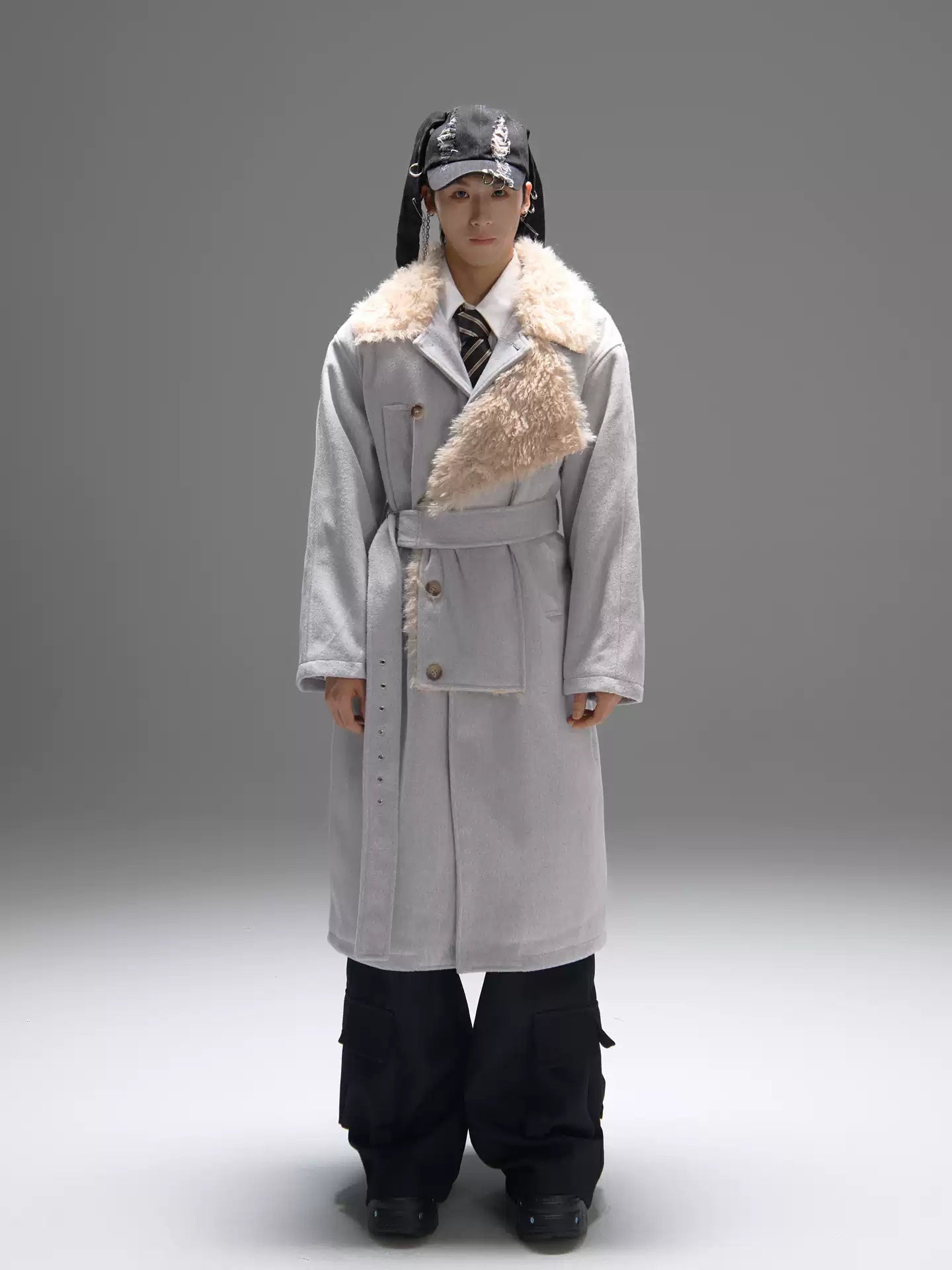 Person wearing a long gray coat with fur trim on a gray background