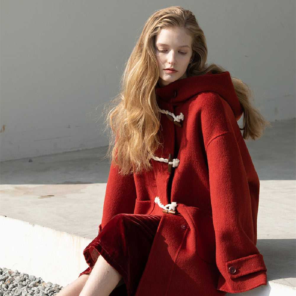 Woman wearing a red coat sitting on a concrete surface with a neutral background