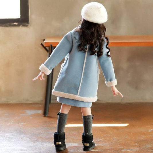 Child wearing a light blue coat with white trim, standing indoors.