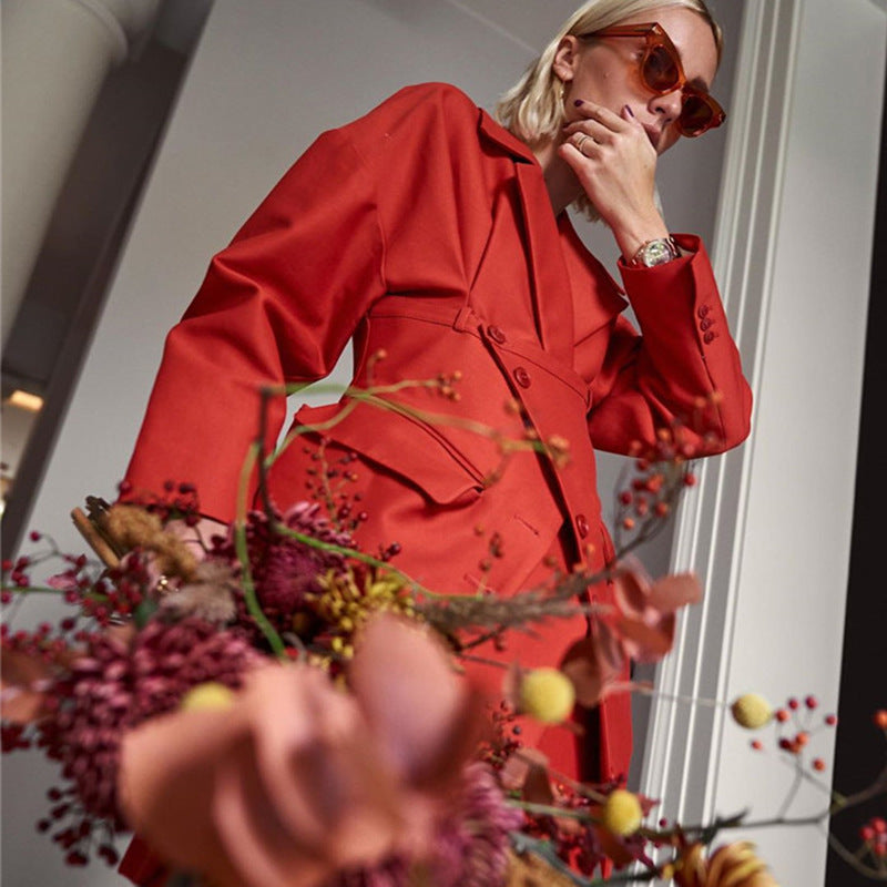 Person wearing a red coat and sunglasses interacting with floral decorations indoors.by millivan