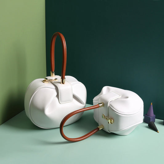 Two white handbags with brown handles on a green surface
