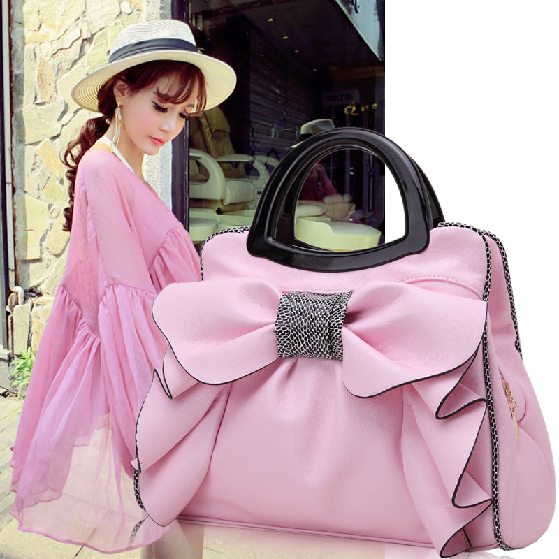 Woman in a pink dress holding a large pink handbag with a bow and black handle.