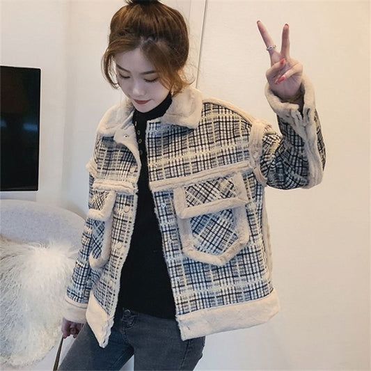 Person wearing a plaid jacket with white fur trim, making a peace sign.