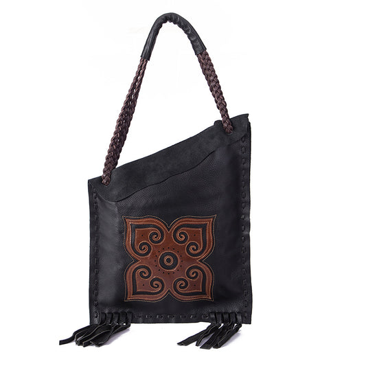 Black leather handbag with braided handle and decorative brown pattern on a white background